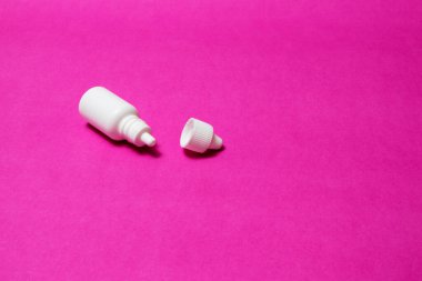 Beyaz bir şişe, göz şişesi ve kırmızı arka planda burun damlası.