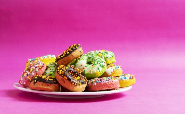 Kırmızı, pembe arka planda beyaz tabakta renkli çörekler.