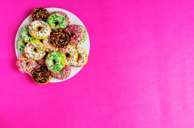 Kırmızı, pembe arka planda beyaz tabakta renkli çörekler.