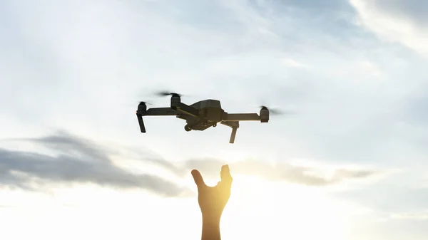 stock image Hand reaching for drone outdoors at sunrise. Testing an aerial unmanned vehicle in nature. Sky background