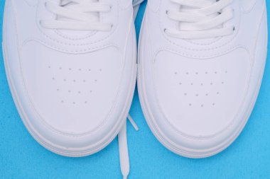 Mavi arka planda bir çift beyaz spor ayakkabı, düz yatıyordu.