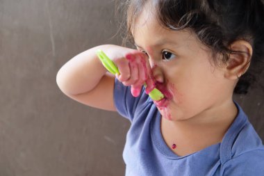 Cute curly boy enjoying exotic dragon fruit with red smudged face