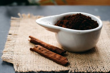 Real coffee grounds in a bowl with cinnamon sticks on a burlap napkin