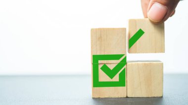 Human hand places a wooden cube with tick icon. Goal achievement and business success. ISO quality and symbols