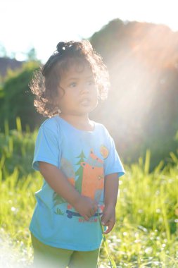 Açık havada gün ışığında duran kıvırcık saçlı bir çocuğun portresi. Yaz parkında poz veren kendine güvenen yakışıklı Asyalı çocuk.