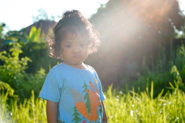 Açık havada gün ışığında duran kıvırcık saçlı bir çocuğun portresi. Yaz parkında poz veren kendine güvenen yakışıklı Asyalı çocuk.