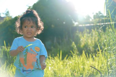 Açık havada gün ışığında duran kıvırcık saçlı bir çocuğun portresi. Yaz parkında poz veren kendine güvenen yakışıklı Asyalı çocuk.