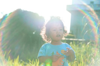 Açık havada gün ışığında duran kıvırcık saçlı bir çocuğun portresi. Yaz parkında poz veren kendine güvenen yakışıklı Asyalı çocuk.