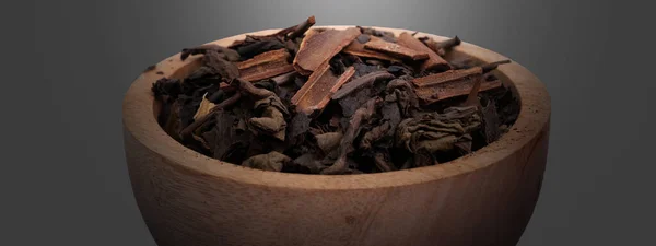 濃い背景の木のボウルにシナモンと乾燥発酵茶葉 — ストック写真