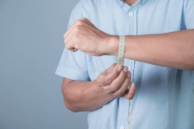 Bir adam bileğini açık mavi arka plan ve kilo verme konseptiyle ölçer.