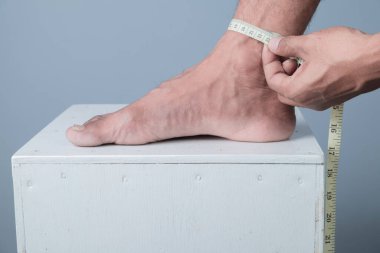 Ayak ölçülerini açık mavi bir arka planla ölçen bir adamın yakın çekimi.
