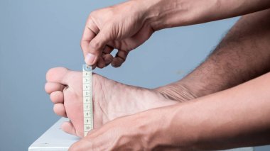 Ayak ölçülerini açık mavi bir arka planla ölçen bir adamın yakın çekimi.