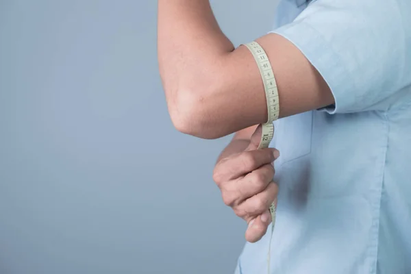 stock image A man measures his wrist with a tape measure on light blue background, weight loss concept