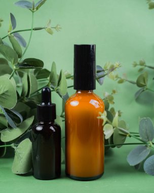 Yeşil arka planda yaprakları olan cam toner ve serum şişeleri. Güzellik ürünü paketleme görüntüsü