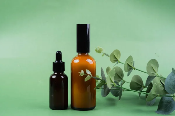 Glass bottles of toner and serum with leaves on green background. Beauty product packaging display