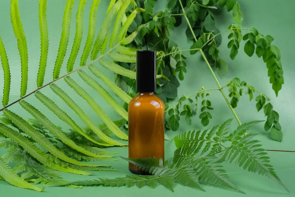 Glass toner bottle with leaves on green background. Beauty product packaging display