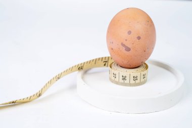 Tavuk yumurtası ve ölçüm bandı beyaz yuvarlak altlık üzerinde metin için fotokopi alanı ile. Diyet ve sağlıklı yaşam kavramı