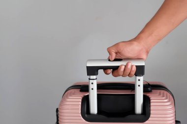 Gri arka planda şeftali rengi bavulu tutan bir erkek. Tatil kavramı