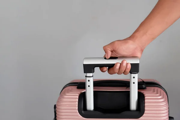 Männliche Hand Hält Einen Pfirsichfarbenen Koffer Auf Grauem Hintergrund Urlaubskonzept — Stockfoto