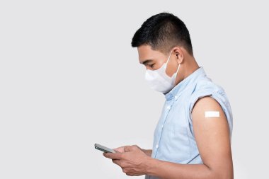 Kolunda bandaj olan aşılı bir Asyalı yetişkin adam akıllı telefon uygulamasında verileri kontrol ediyor. Virüslere karşı koruma.