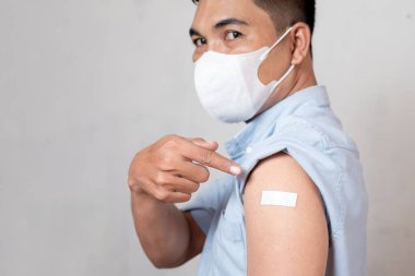 Aşılanmış Asyalı yetişkin bir adam antivirüs enjeksiyonundan sonra kolunda yapıştırıcı bandaj gösteriyor. Aşıyı buldum.