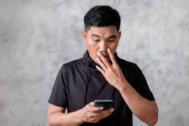 Akıllı telefon tutan, ağzı eliyle kapatan, şok olmuş ve hata yapmaktan korkan kendine güvenen Asyalı genç adam. şaşırmış ifade
