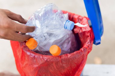 Erkek eli boş plastik su şişesini geri dönüşüm kutusuna atıyor.