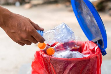 Erkek eli boş plastik su şişesini geri dönüşüm kutusuna atıyor.