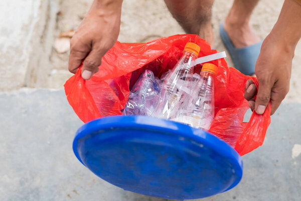 Male hand throwing empty plastic water bottle into recycling bin