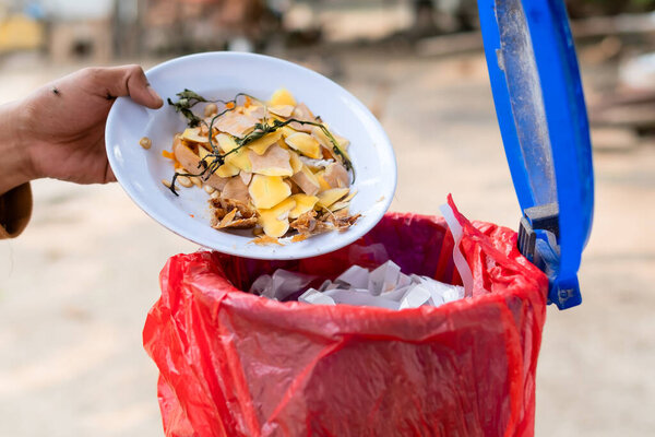Close-up of Asian man's hand pouring leftover food from plate into trash