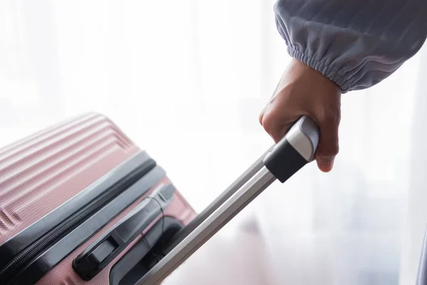 An Asian woman\'s hand pulls the handle of a suitcase isolated on a white background. Travel and tourism concept.