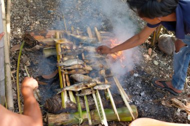 Bir adamın eli ızgara balığı dumanlı kömürlerin üzerinde çevirir.