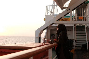 Güverteden gün batımına bakan bir kadın yolcu. Asyalı kız turist dışarıda dinleniyor. Manzaranın tadını çıkarıyor..