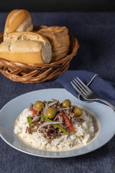 Shredded meat with rice and olives, typical Cuban food on blue tablecloth.