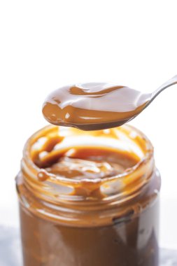 Spoon scooping dulce de leche out of a jar, traditional sweet from Argentina isolated on white background.