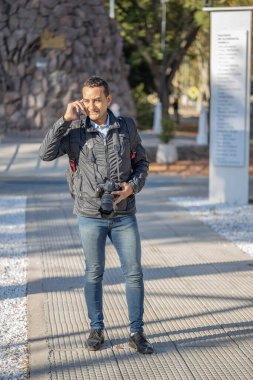 Boynunda fotoğraf makinesiyle cep telefonuyla konuşan genç bir latin..