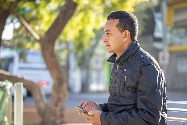 Mladý Latinský Muž Sedí Hranaté Lavičce Pomocí Mobilního Telefonu — Stock fotografie
