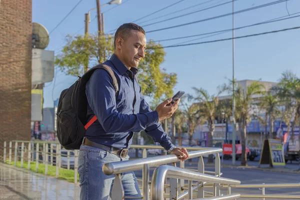 Mladý Latinský Muž Batohem Při Pohledu Svůj Mobilní Telefon — Stock fotografie