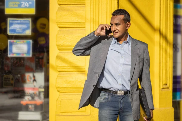 Portrét Mladého Latinskoamerického Muže Mluvícího Přes Žlutou Zeď Mobilním Telefonu — Stock fotografie