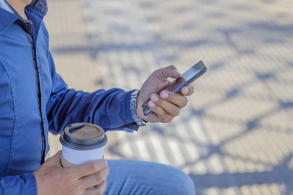 stock image Detail of the hands of a man with a mobile phone and a paper cup of coffee.