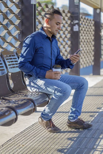Mladý Latinský Muž Sedí Čeká Autobus Dívá Svůj Mobilní Telefon — Stock fotografie