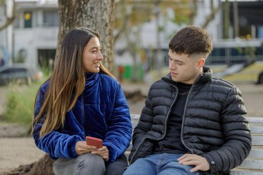 Halka açık bir parkta bankta oturan bir çift kız ve oğlan..