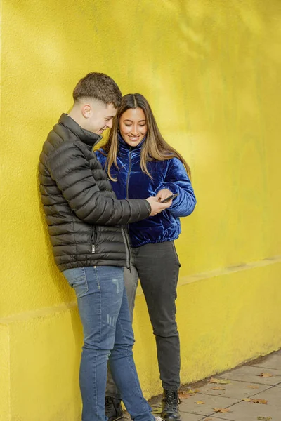 Młoda Para Szuka Telefonu Komórkowego Żółtą Ścianą Tle — Zdjęcie stockowe