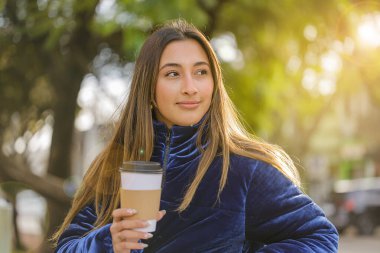 Güzel Latin kız halka açık bir bankta fotokopi alanı olan kahve içiyor..