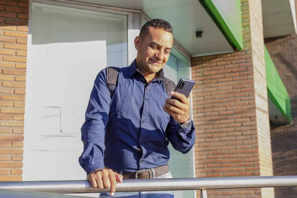 Usmívající Mladý Latinský Muž Dívá Svůj Mobilní Telefon — Stock fotografie