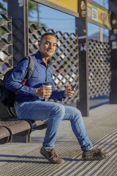 Mladý Latinský Muž Sedí Čeká Autobus Papírovým Šálkem Kávy Ruce — Stock fotografie