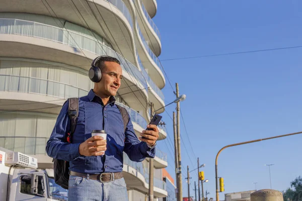 Kulaklıklı genç bir latin cep telefonuna bakıyor ve elinde fotokopi alanı olan bir kahve bardağı tutuyor..