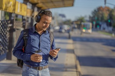 Otobüs durağında cep telefonuna bakan kulaklıklı genç bir latin..