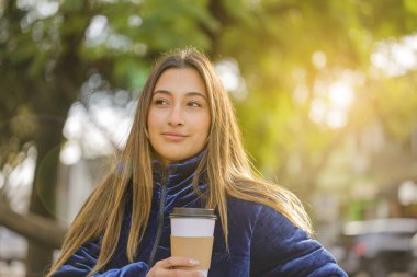 Güzel Latin kızın portresi halka açık bir bankta fotokopi alanı olan kahve içiyor..