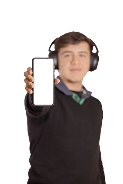 焦点を絞ったヘッドフォンを持つ白人の少年は 白い背景に隔離された彼の携帯電話の空白の画面を示しています — ストック写真